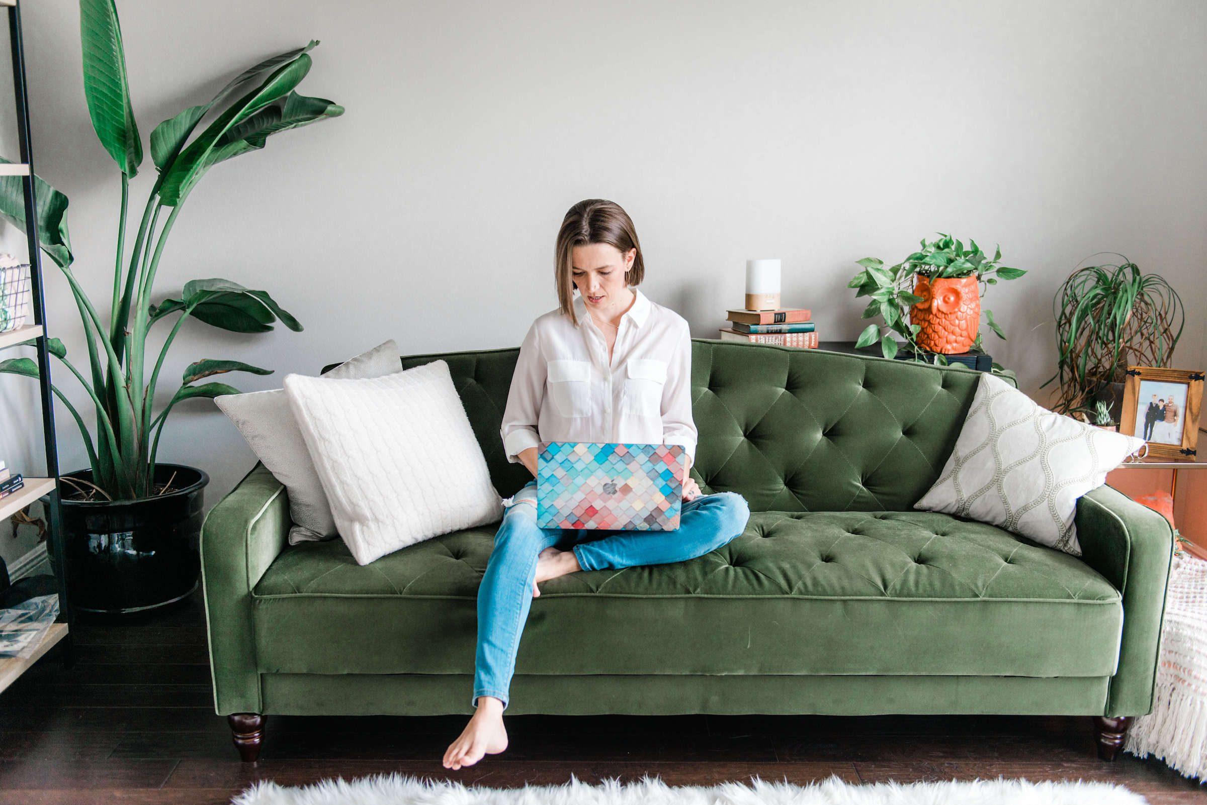 Tara sitting on green pin-tucked couch on laptop