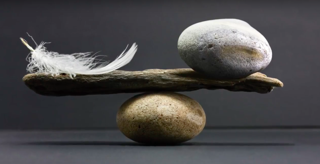 rock and feather being balanced on a stick and a rock