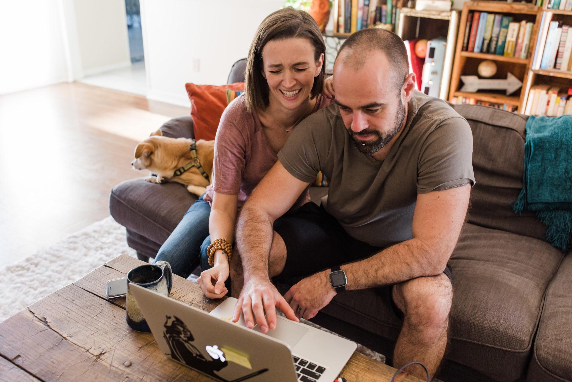 Tara and Justin laughing as they look at the laptop from their couch