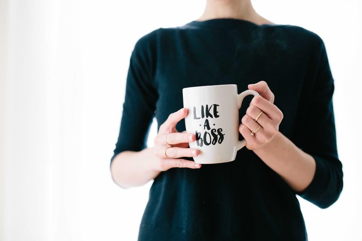 Woman in black 3/4 sleeve shirt holding a white mug that says "LIKE A BOSS".