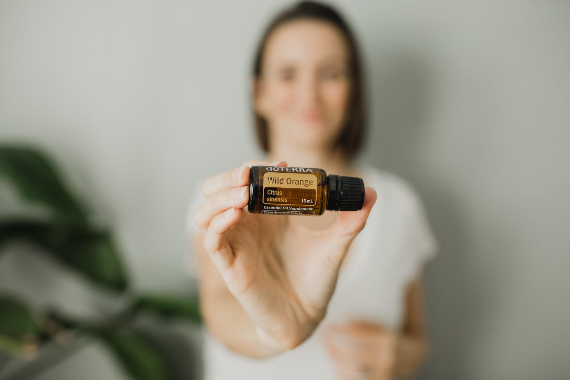 Tara out of focus holding Wild Orange essential oil bottle focused