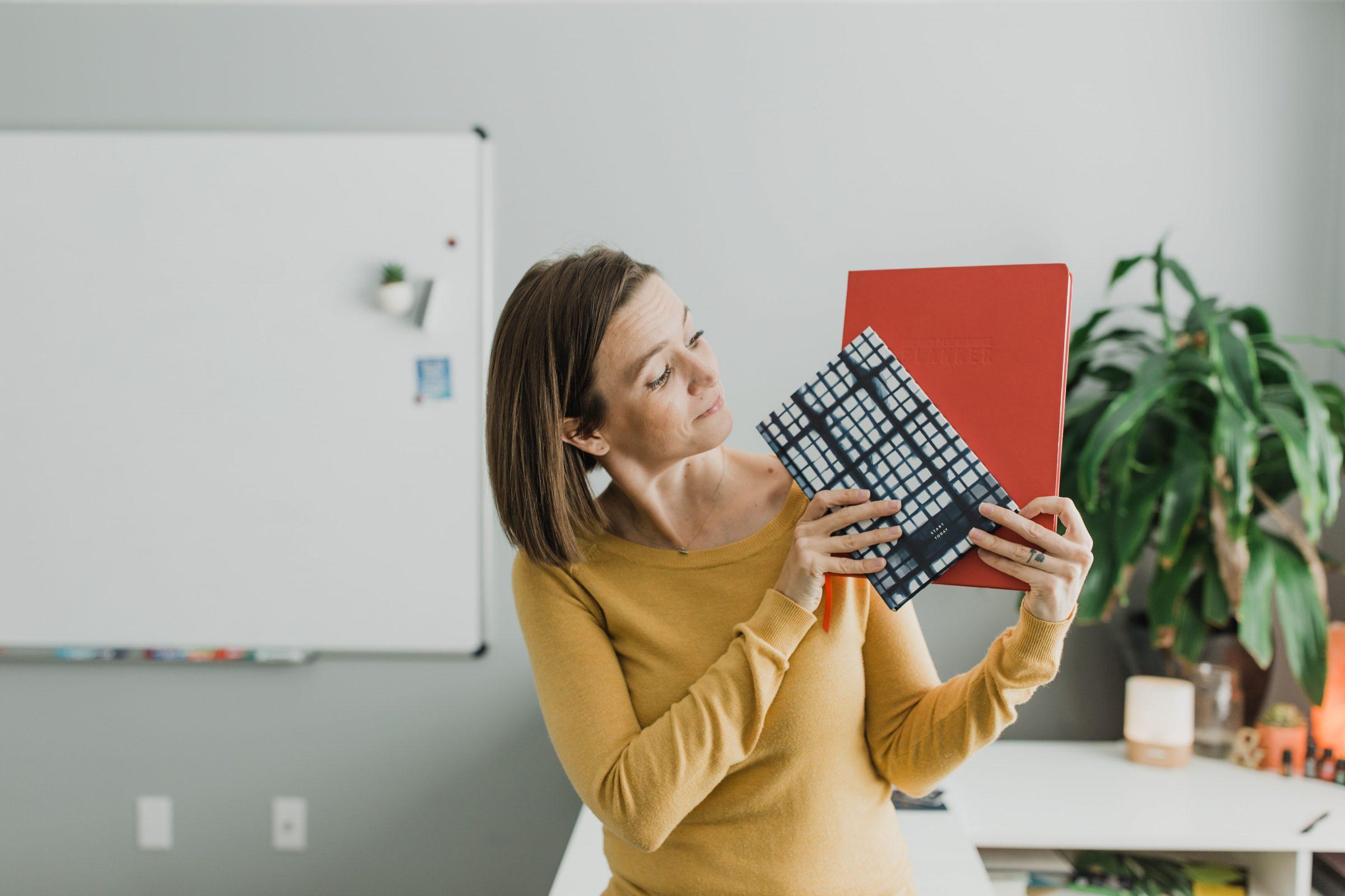 Tara in mustard long-sleeve shirt in office holding up 2 planners