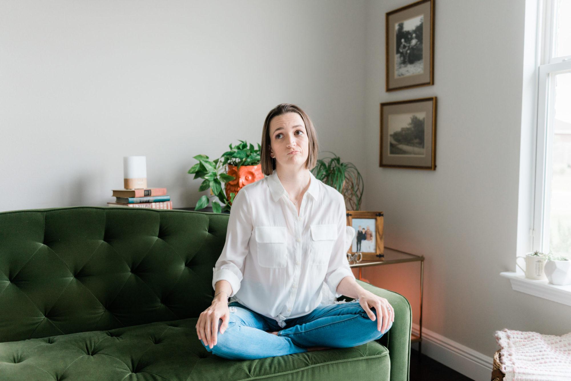 Tara sitting on emerald pin-tucked couch thinking