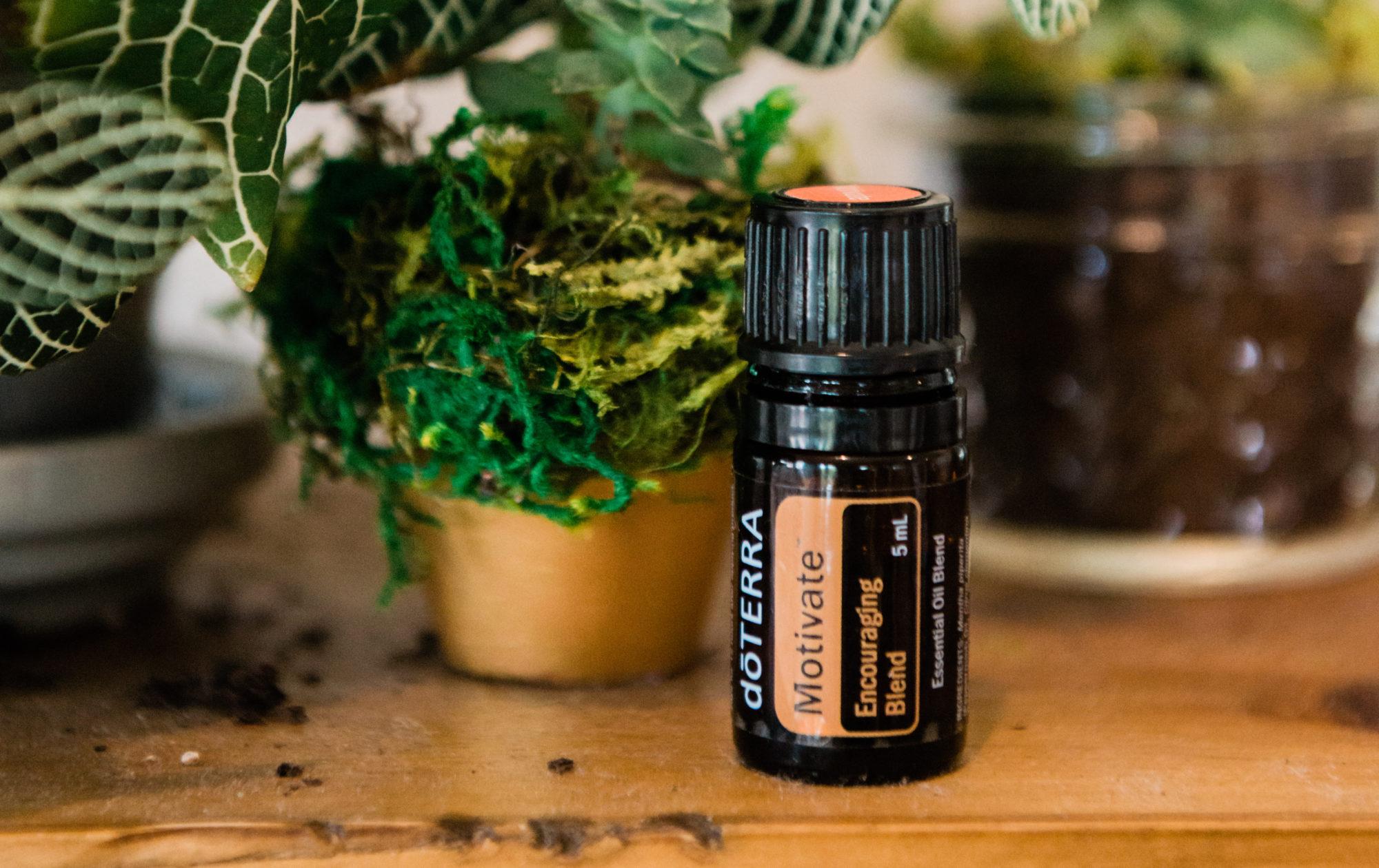 Motivate Essential oil on wood table with green plants in the background