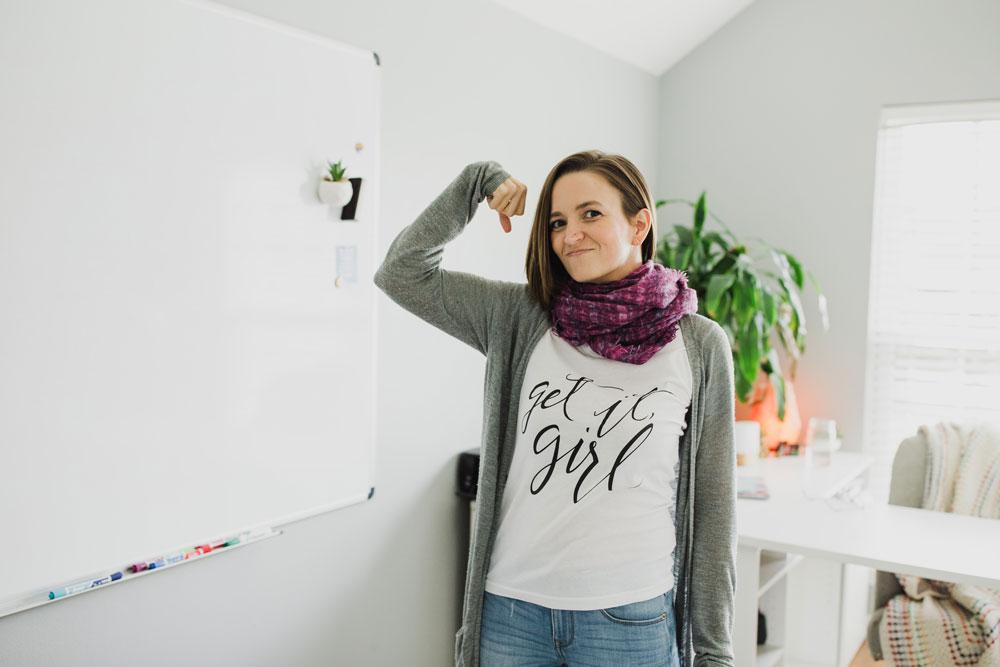 Tara in home office wearing "get it girl" shirt flexing one arm