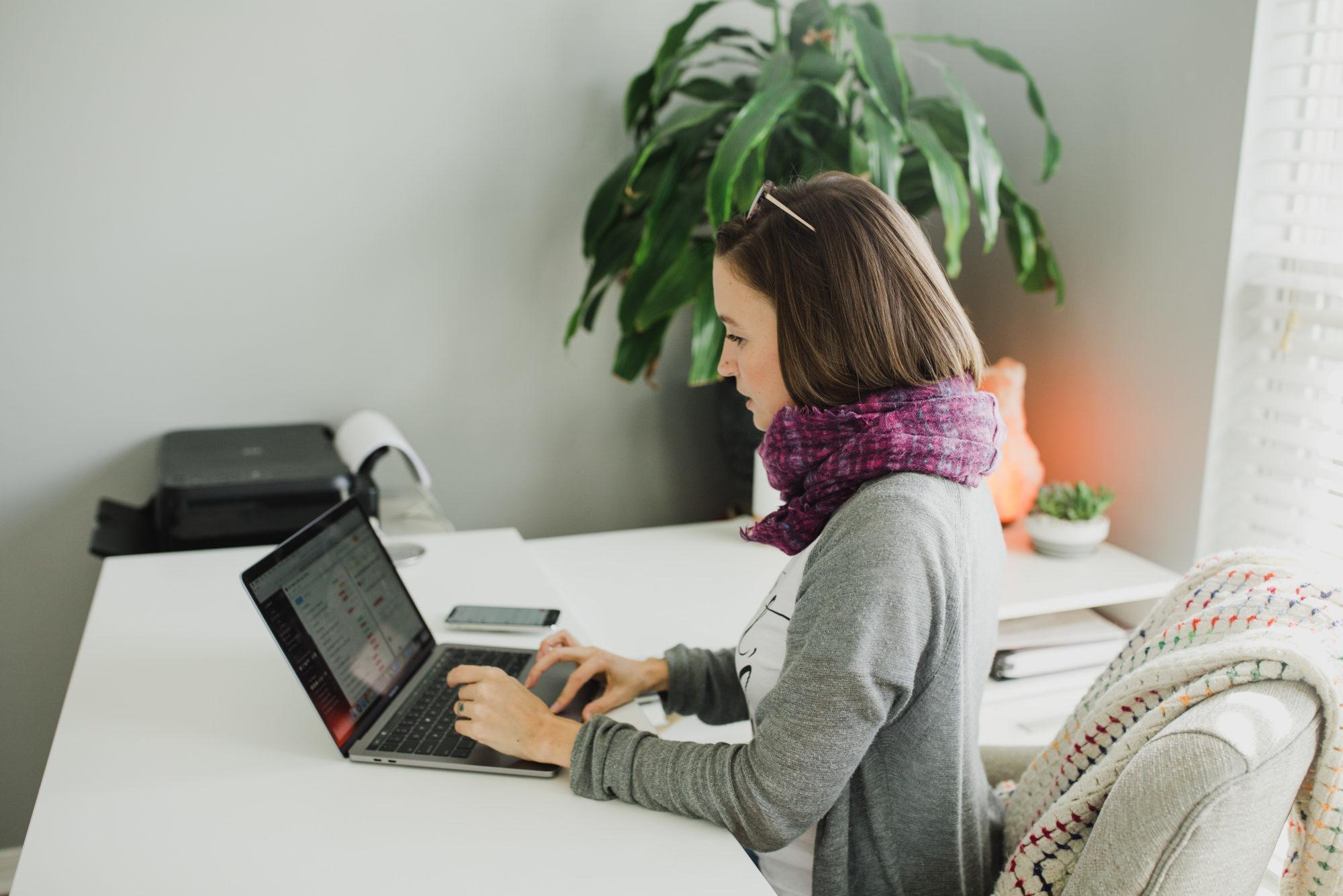 Tara working on laptop in home office weaing gray cardigan and purple scarf