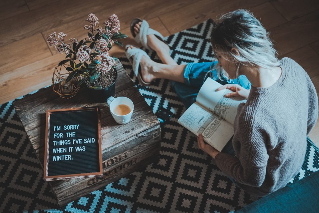 Girl sitting on floor with book in hand and letterboard that says "I'm sorry for the things I've said when it was winter"