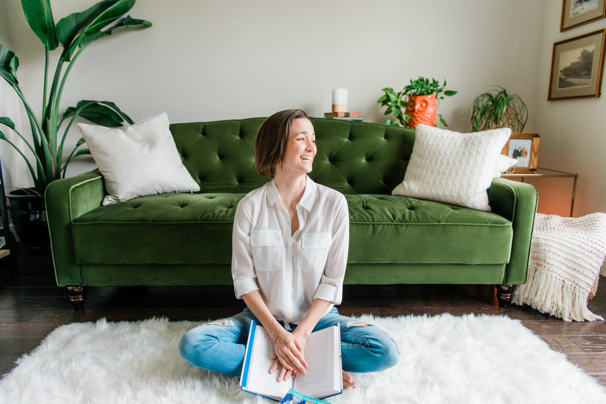 Tara sitting on the ground laughing with book in hand, emerald couch in the background