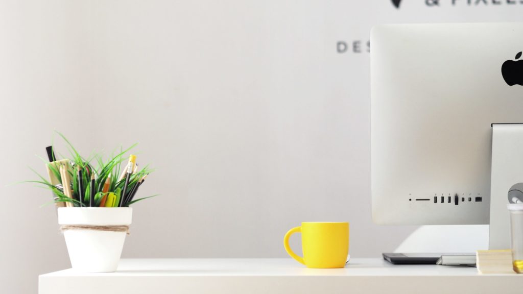 minimalist white desk, computer, yellow coffee mug and plant with pencils
