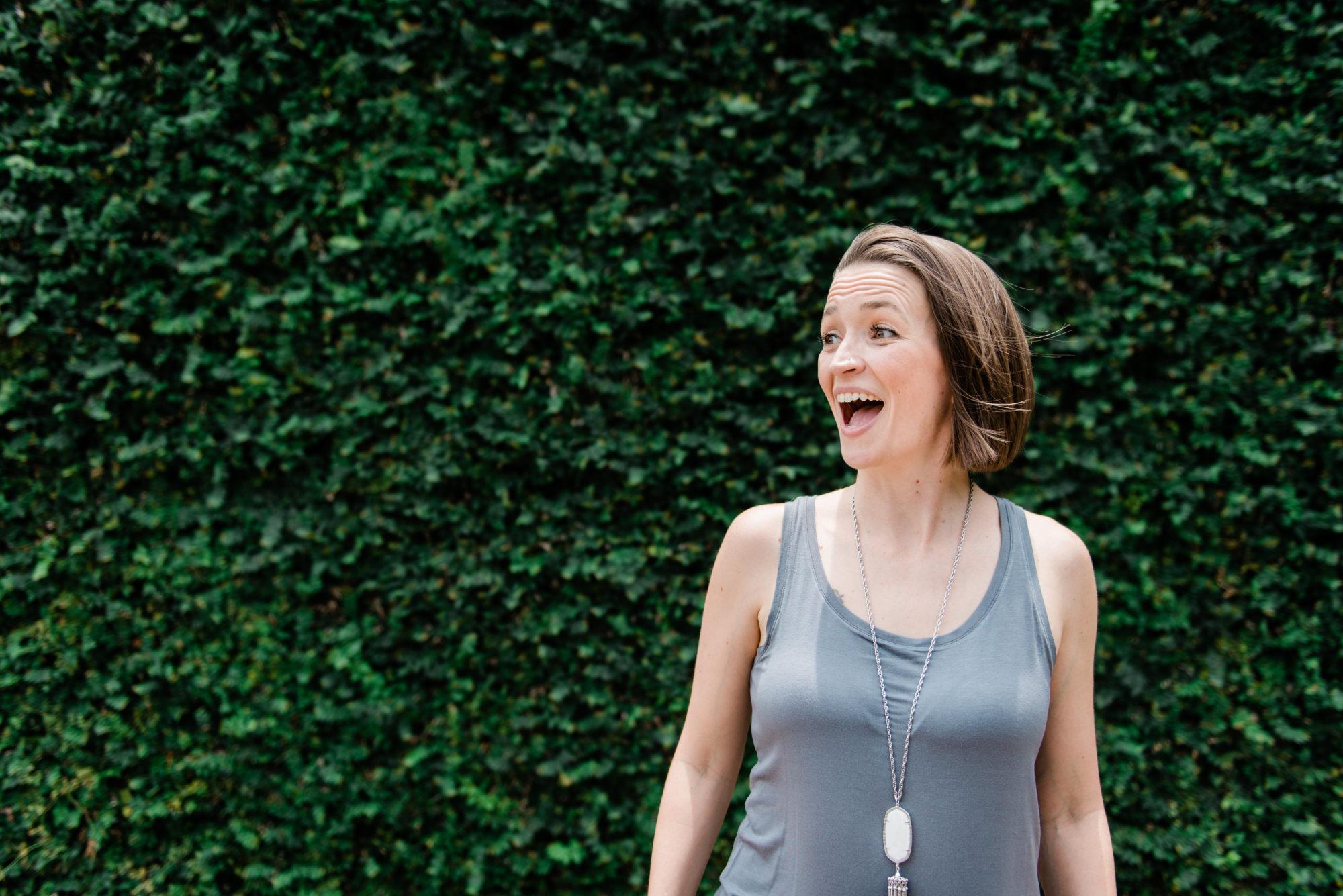 Tara excited wearing a gray tank top with a backdrop of deep green leaves