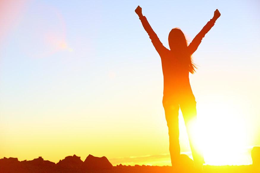 woman with celebratory arms up silhouetted by the sun