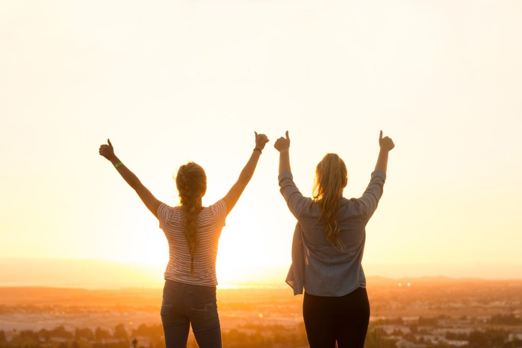 2 women side by side celebrating silhouetted by the sun