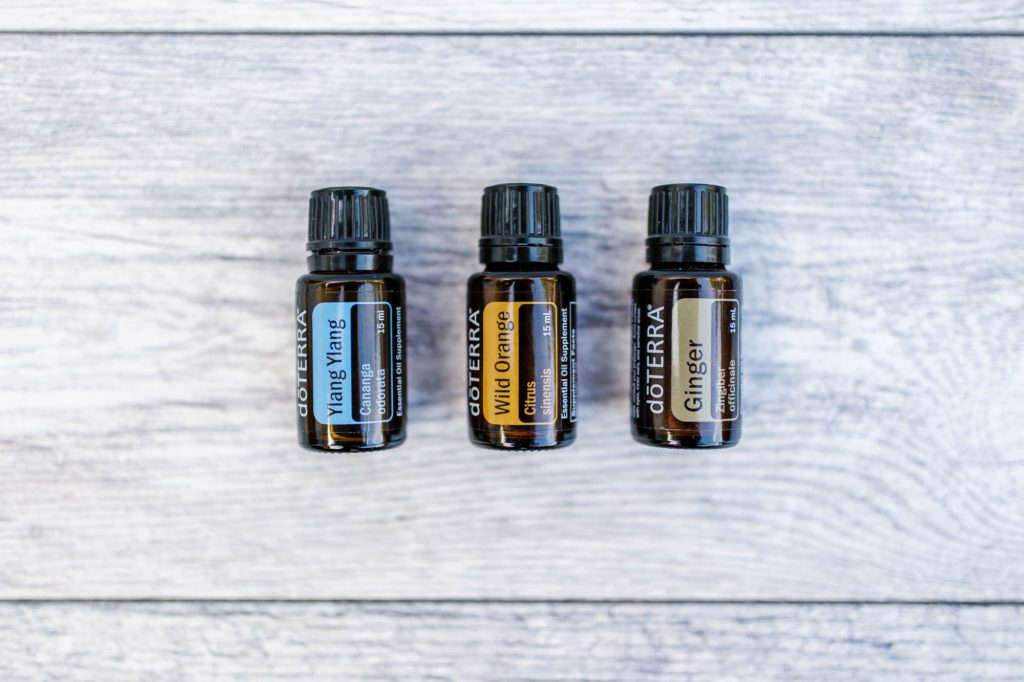 Ylan Ylang, Wild Orange, and Ginger essential oils laid flat beside each other on wood table