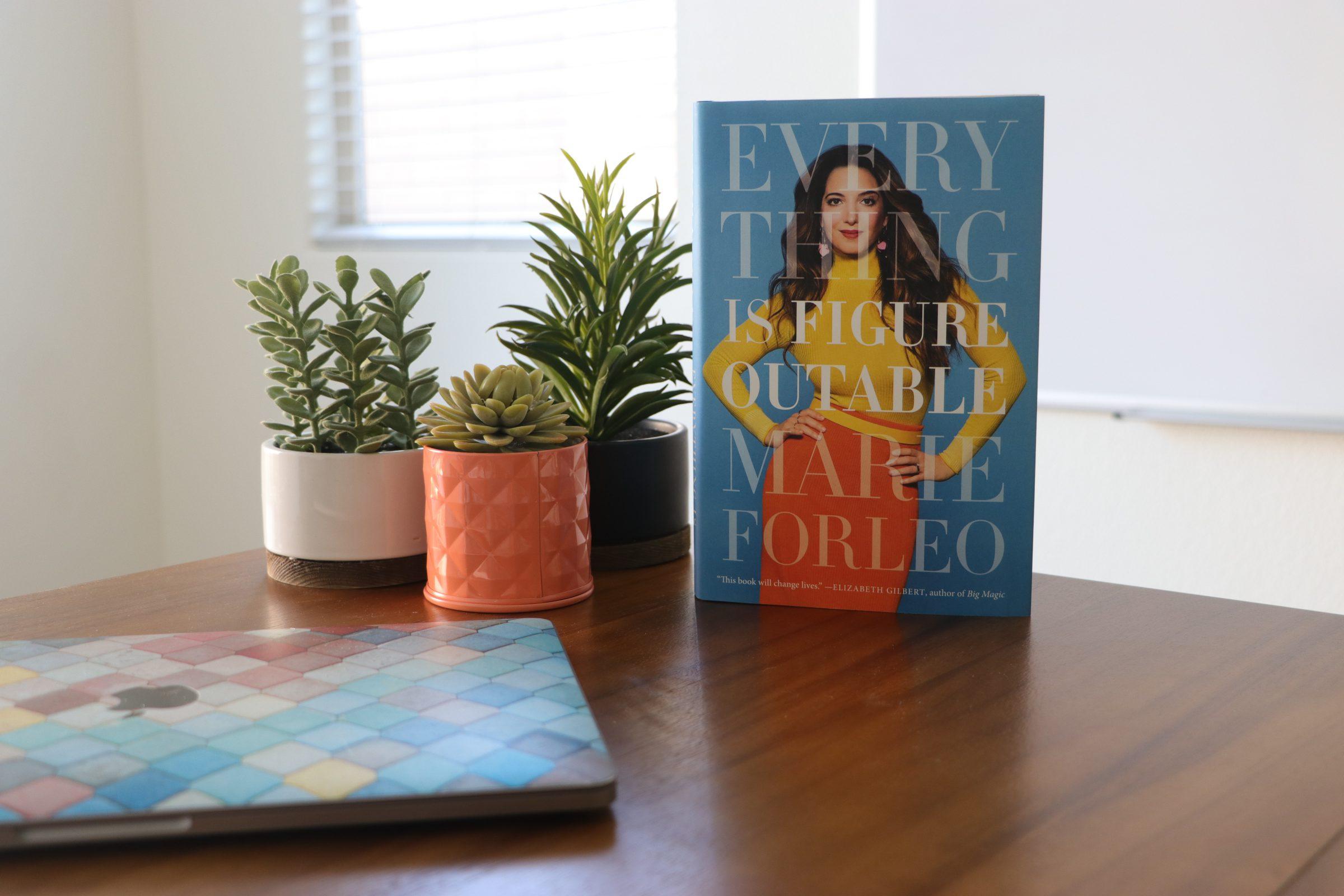 Marie Forelo's book Everything is Figureoutable sitting on desk beside plants and laptop