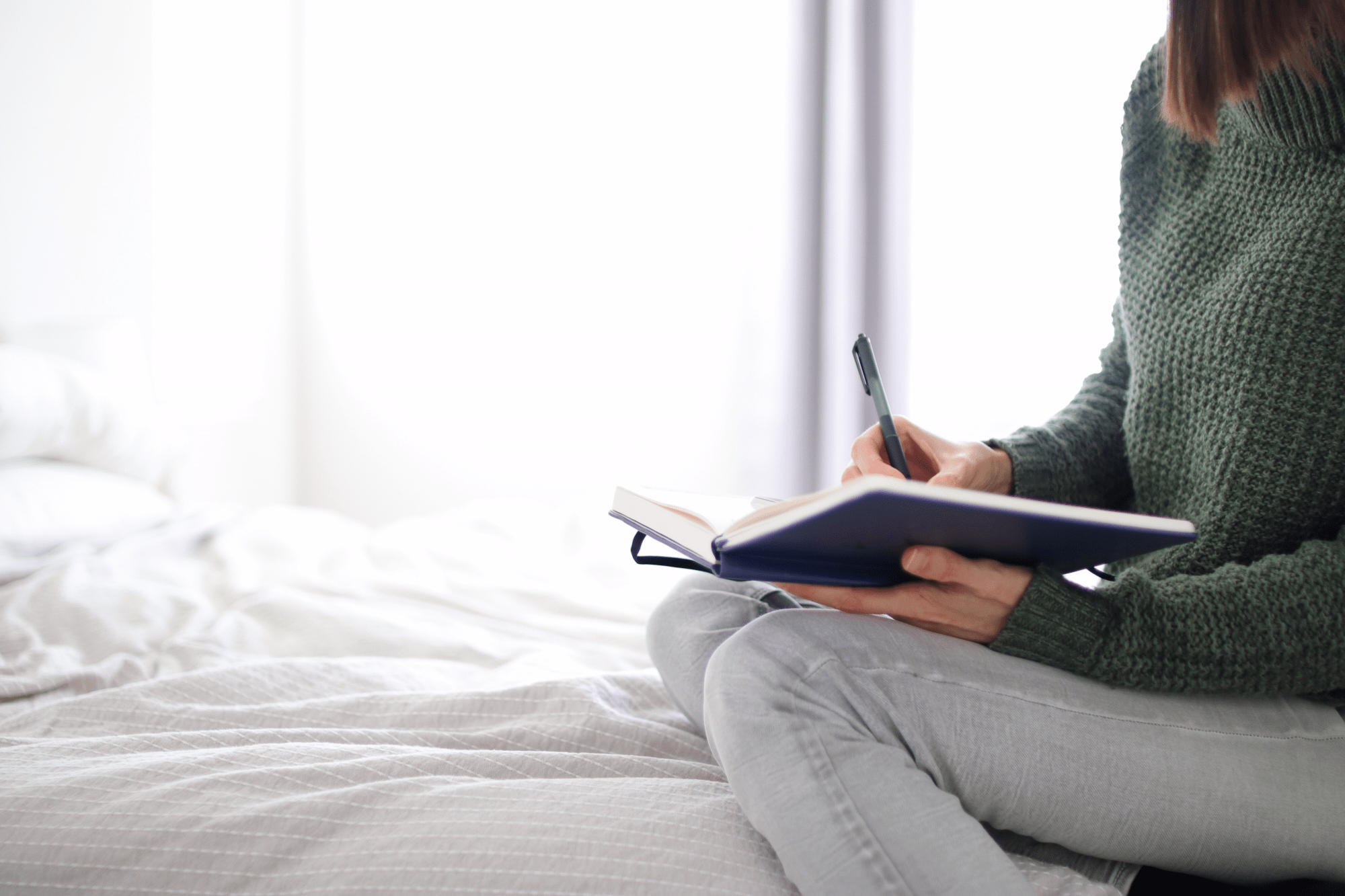 Tara sitting on white bed writing in journal