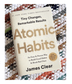 Gold and beige paperback book that reads in bold gold font "Atomic Habits" placed on top of a multicolored rug