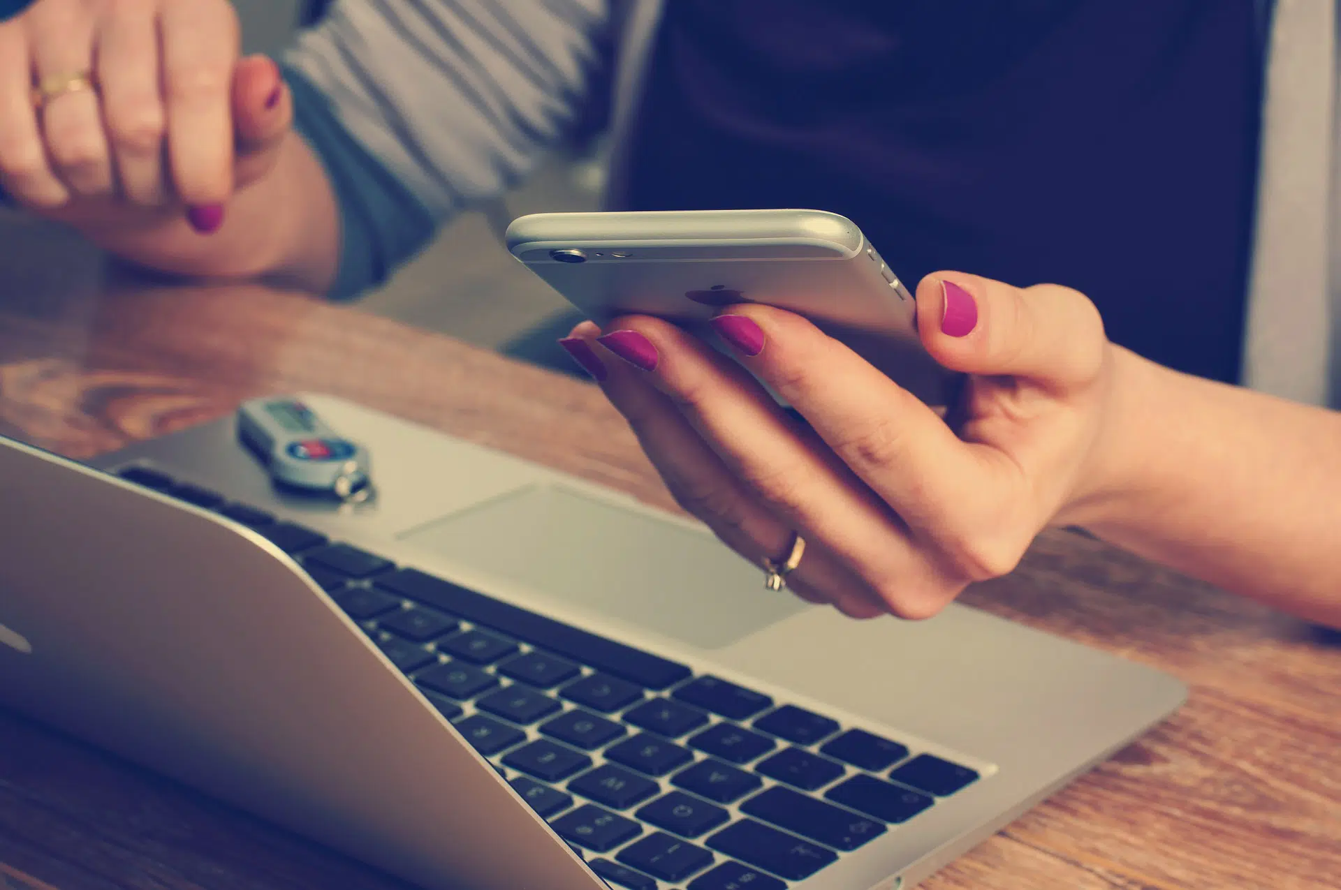 A woman in front of her computer, holding her phone in her hand