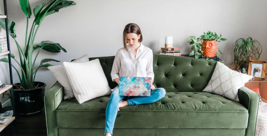 Tara sitting on green pin-tucked couch on laptop