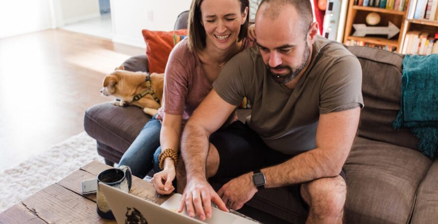 Tara and Justin laughing as they look at the laptop from their couch
