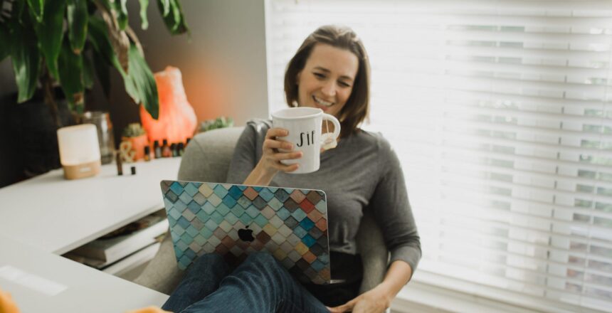 Taa sitting at with her feet on her desk as she laughs and sips tea with laptop on her lap