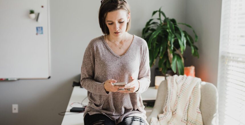 Tara leaning on desk in scrolling through phone