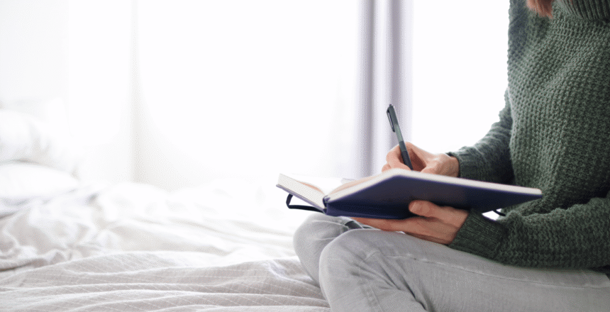 Tara sitting on white bed writing in journal