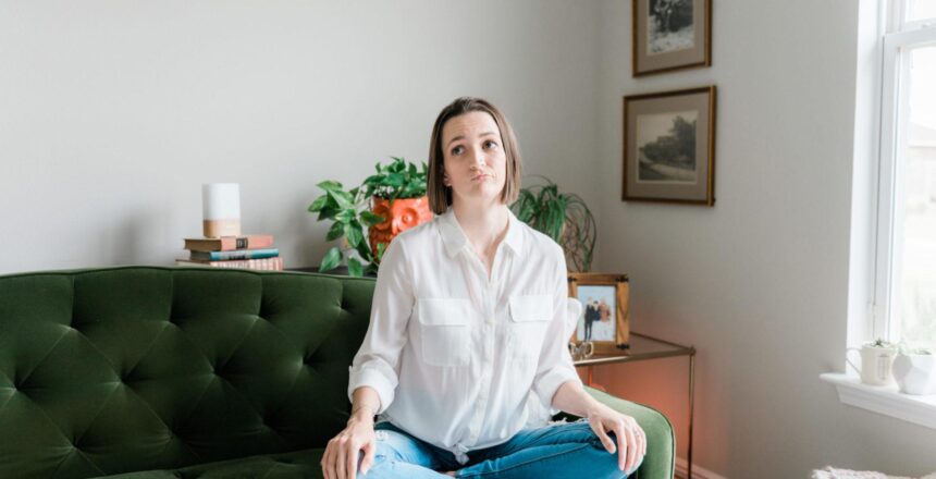 Tara sitting on emerald pin-tucked couch thinking