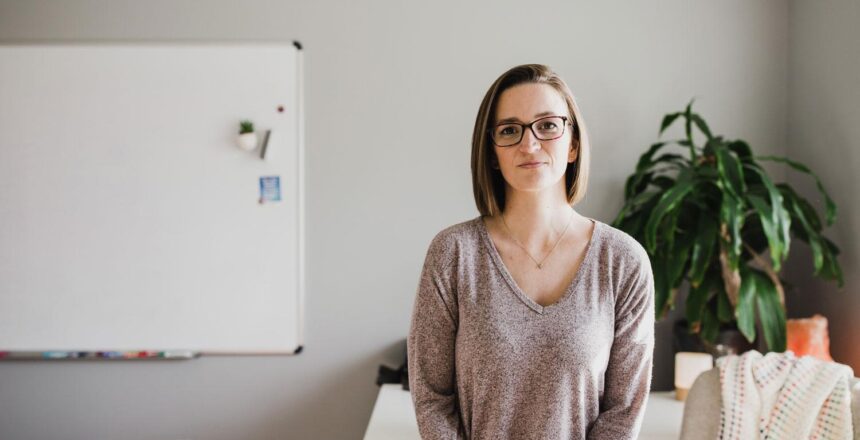 Tara in long sleeve gray tri-blend long sleeve shirt sitting on her desk in her office