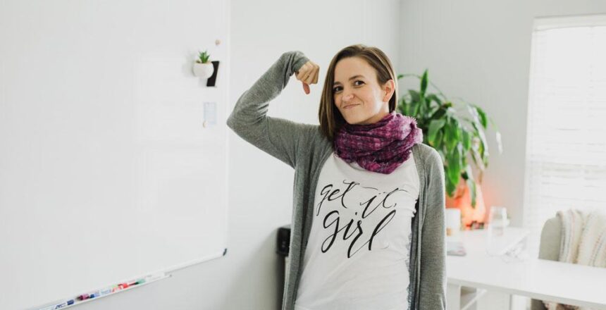 Tara in home office wearing "get it girl" shirt flexing one arm