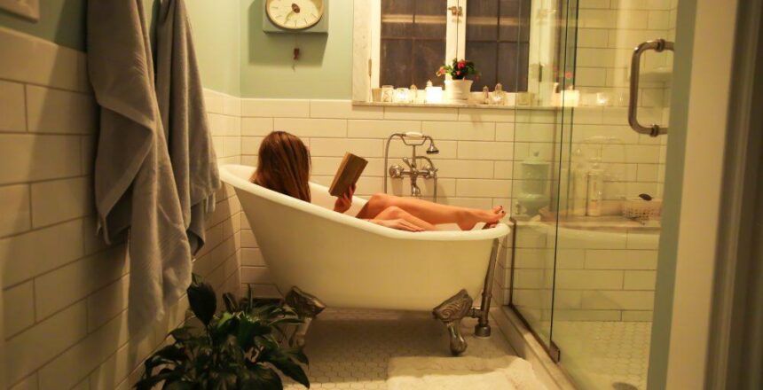 Woman in white ceramic bathtub reading.