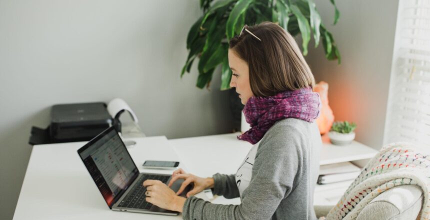 Tara working on laptop in home office weaing gray cardigan and purple scarf