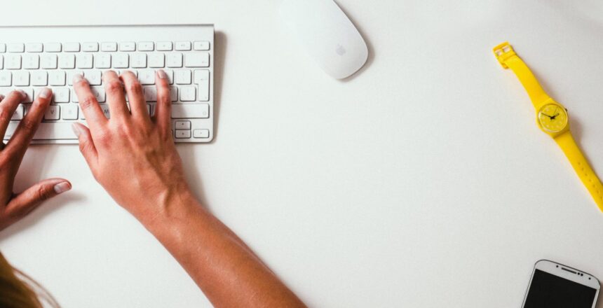Person working at computer keyboard with watch and phone on table
