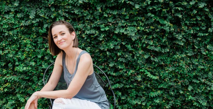 tara sitting casually smiling with a lush green leagy background