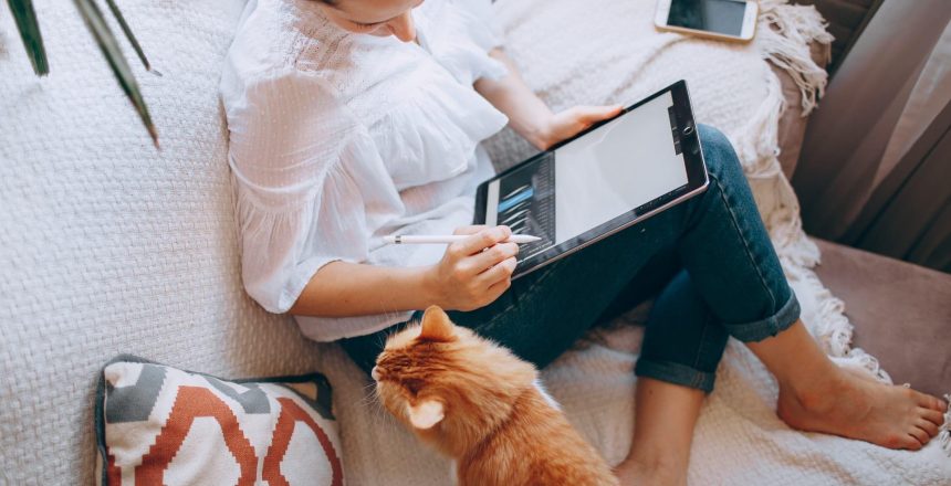 a young woman and her cat on the couch reading from her ipad