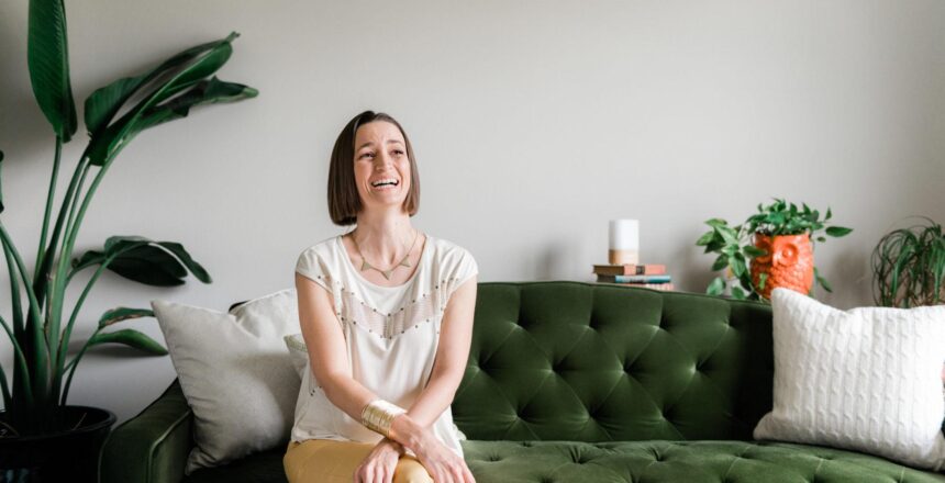 Tara sitting and laughing on green pin-tucked couch beside large house plant