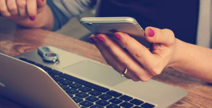 A woman in front of her computer, holding her phone in her hand