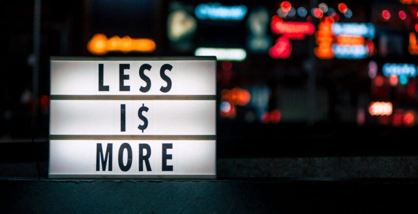 a luminated sign with the 3 rows. First row says "less." Second row say "is." And, the third row says "more." Behind the sign is a big city with lights.
