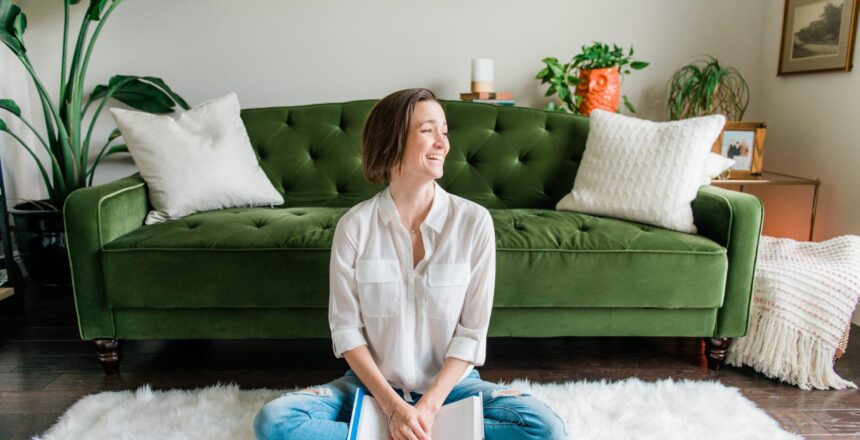 Tara sitting on the ground laughing with book in hand, emerald couch in the background