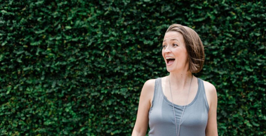 Tara excited wearing a gray tank top with a backdrop of deep green leaves